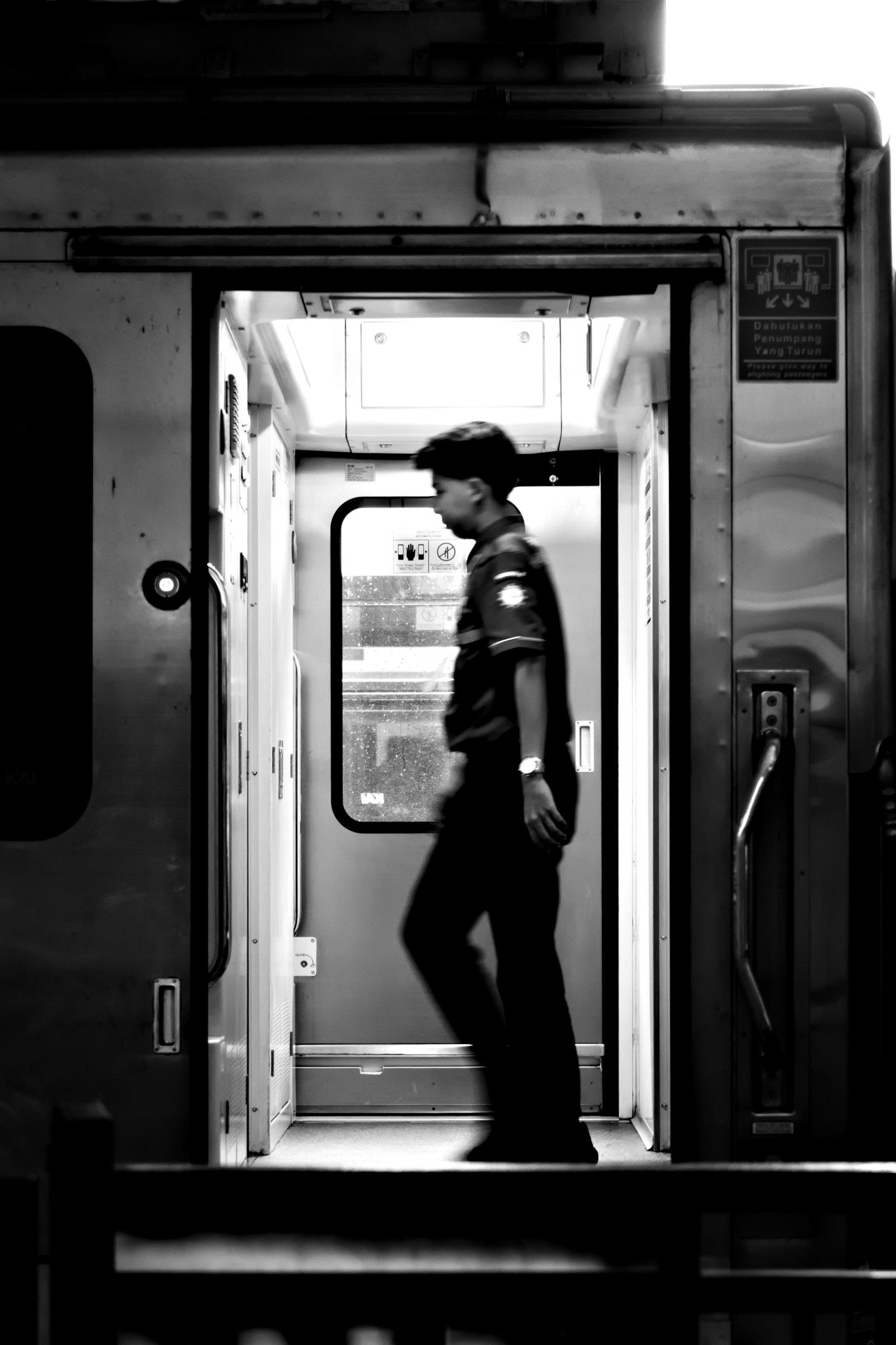 A B&W photo of a train maintenance personnel passing through a car, as seen through an open door.